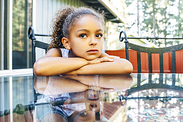 Pensive Mixed Race girl leaning on glass table