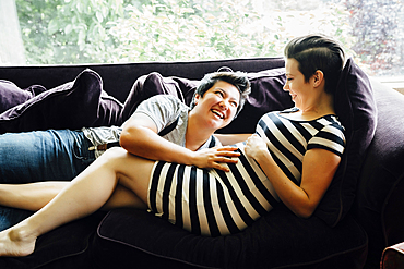 Pregnant lesbian couple cuddling on sofa