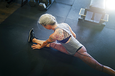 Caucasian woman stretching leg on gymnasium floor