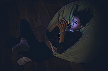 Mixed Race girl using cell phone laying on bean bag in dark