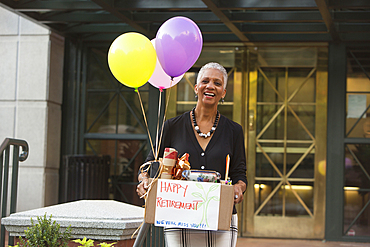 Black woman carrying belongings with happy retirement sign and balloons