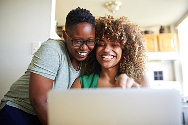 Laughing Black women hugging and using laptop