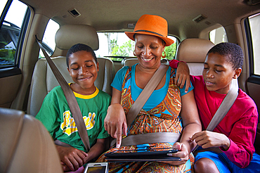 Black mother and twin sons using digital tablet in car