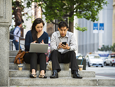 Chinese business people using technology during lunch in city