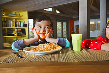 Sister watching Mixed Race brother with messy face eating spaghetti