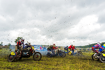 Caucasian racers on motorcycles with side cars spraying dirt