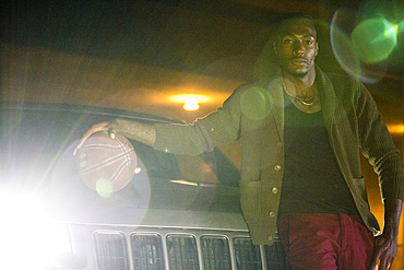 Headlights shining on Black man playing basketball