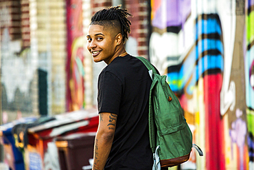 Portrait of smiling androgynous Mixed Race woman near on graffiti wall