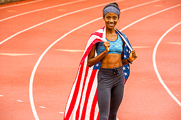 Smiling Black athlete posing with American flag on track