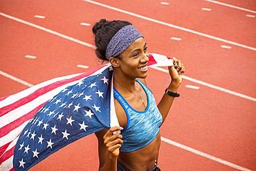 Smiling Black athlete holding American flag on track