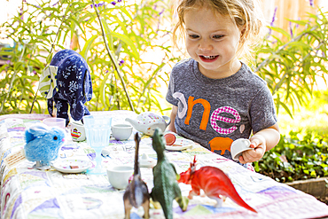 Caucasian girl playing with tea set and dinosaurs