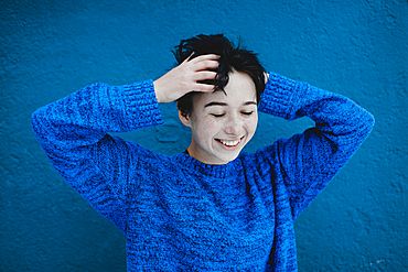 Smiling Caucasian woman tousling hair near blue wall