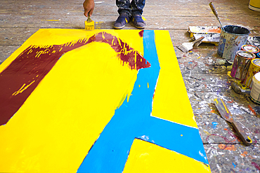 Legs of Mari man painting canvas on floor