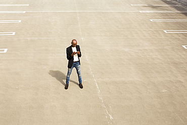 Gay Black man texting in empty parking lot