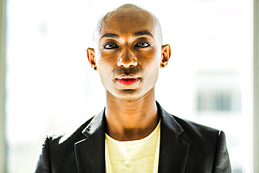 Serious gay Black man posing near window