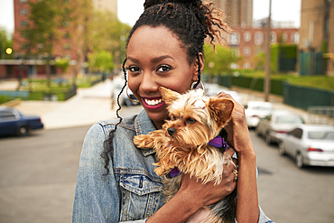 Black woman holding dog in city