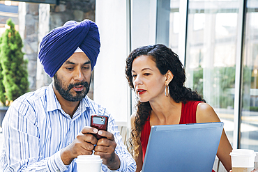 Man and woman using cell phone and laptop at cafe