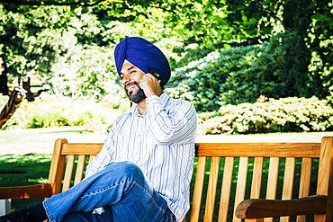 Man wearing turban sitting on park bench talking on cell phone