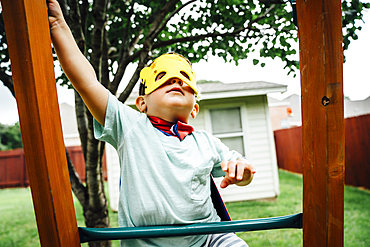 Caucasian boy wearing superhero costume climbing on backyard playground