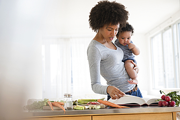 Mother reading cookbook while holding baby son