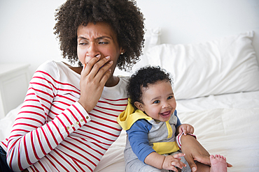 Mother yawning on bed holding baby son