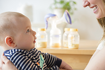 Caucasian woman holding baby son near bottles of breast milk