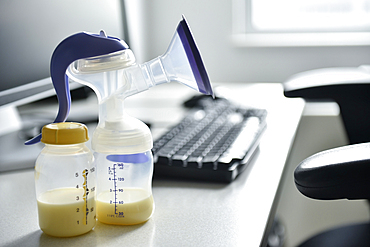 Breast pump and bottle of breast milk near computer