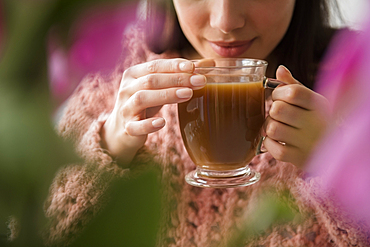 Hispanic woman drinking coffee behind flowers