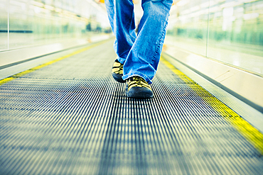 Legs of Japanese woman wearing jeans walking on moving walkway