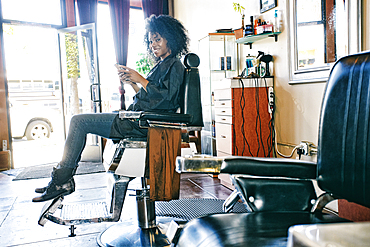 Smiling Black hairdresser texting on cell phone in hair salon