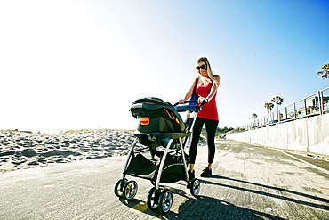 Mother pushing baby son in stroller at beach