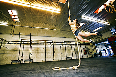 Mixed Race woman climbing rope in gymnasium