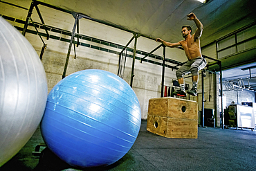 Caucasian man jumping on wooden crate in gymnasium