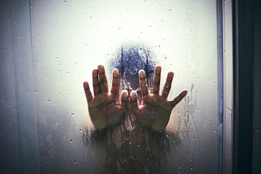 Hands of Hispanic boy leaning on shower door