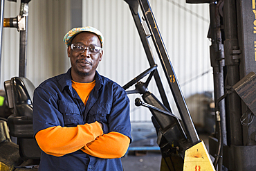 Smiling Black worker posing near forklift in factory