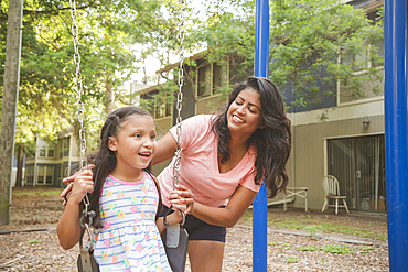 Hispanic mother pushing daughter in playground swing