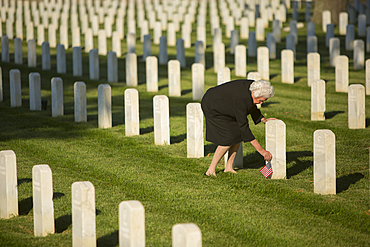 Caucasian widow placing American flag at cemetery gravestone