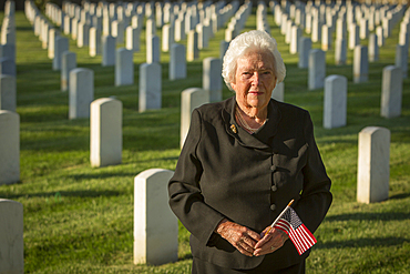 Caucasian widow holding American flag in cemetery