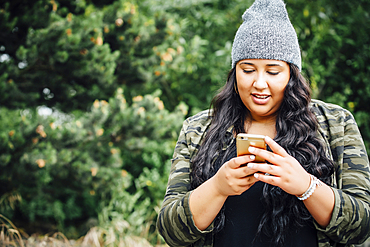 Mixed Race woman texting on cell phone in forest