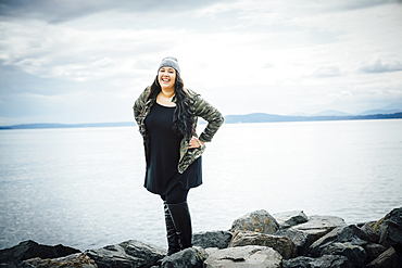 Smiling Mixed Race woman posing on rocks near ocean