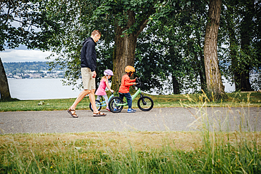 Father watching daughter and son riding bicycles