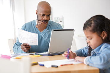 Daughter coloring with crayons while father uses laptop