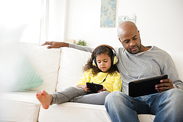 Father and daughter using digital tablets on sofa