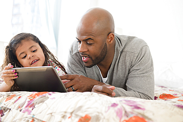 Father and daughter using digital tablet on bed