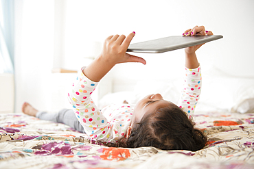 Mixed Race girl laying on bed using digital tablet