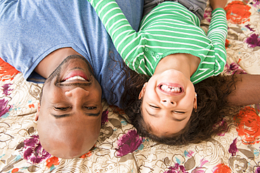 Smiling father and daughter laying on bed