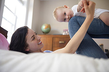 Caucasian mother laying on bed balancing baby son on legs