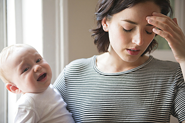 Caucasian mother rubbing forehead while holding baby son