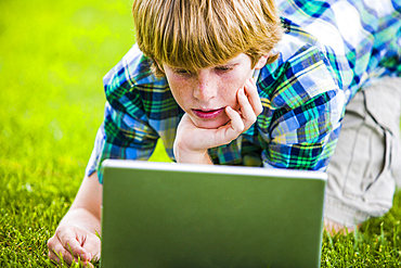 Caucasian boy kneeling in grass using laptop