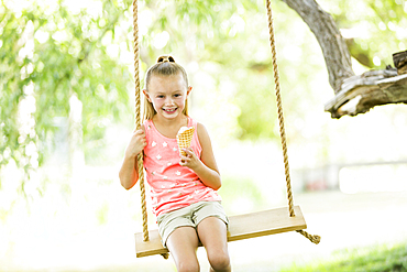 Caucasian girl eating ice cream cone on rope swing